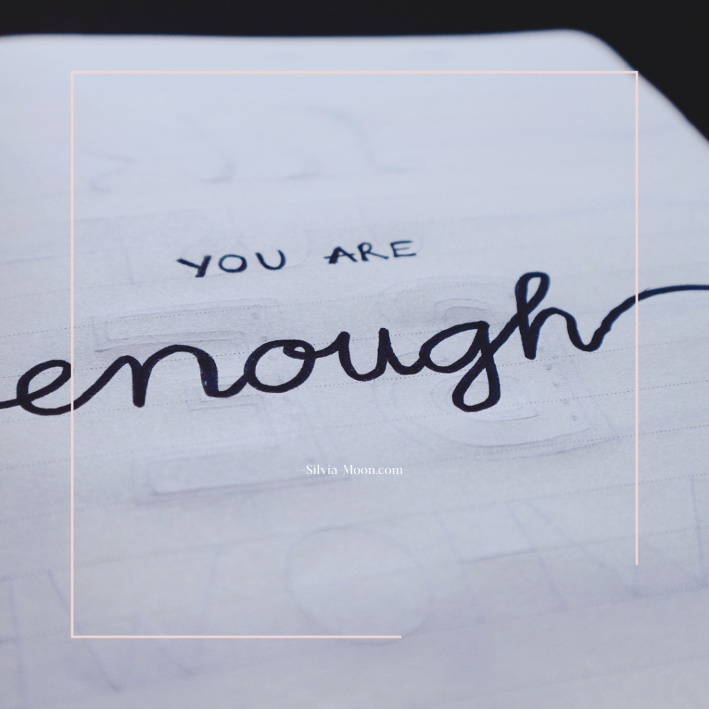 Close-up of handwritten text that reads 'YOU ARE enough' on an open notebook page.